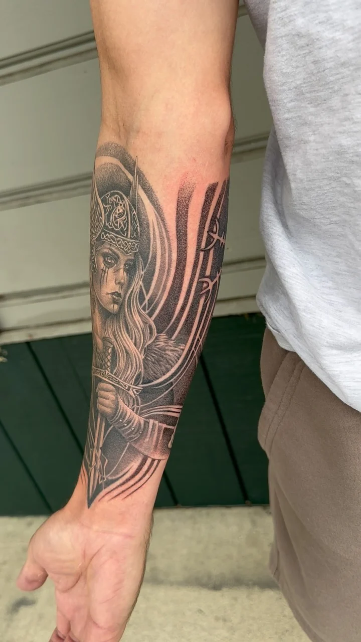 The video poster shows a detailed female warrior portrait with a helmet, flowing hair, and ornamental arcs wrapping a forearm. Tattoo work by Brian of Vicious Ink.