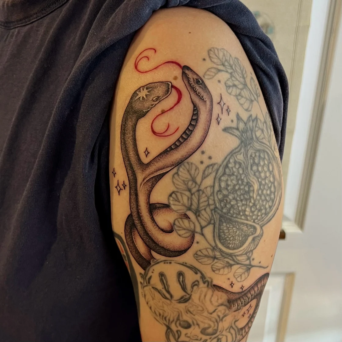 A shaded snake with red accents curves beside a circular ornamental pattern and botanical details on the upper arm. Tattoo work by Abra of Vicious Ink.